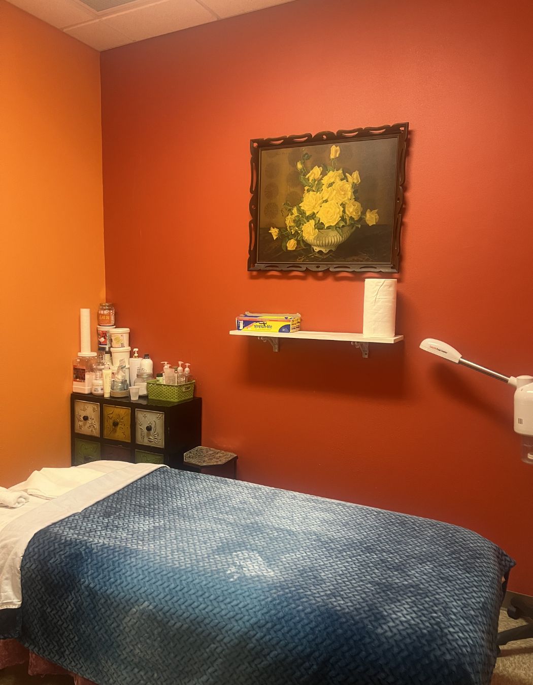 Massage table in a treatment room at Taichi Spa in San Antonio, Texas, featuring an orange accent wall and a blue blanket for a vibrant, calming atmosphere.